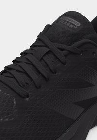 Κοντινό πλάνο μαύρου αθλητικού παπουτσιού New Balance με υφασμένο δίχτυ, χοντρές κορδόνια και την επιγραφή «FLASH» στη γλώσσα.