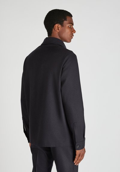 Giacca in lana blu scuro con colletto, polsini bottonati e taglio dritto. Il tessuto testurizzato ha una finitura liscia con dettagli minimi.