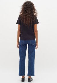 T-shirt noir à manches courtes associé à un jean droit bleu. Le jean présente un délavage moyen et des détails de couture subtils sur les poches arrière.