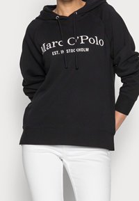 Felpa nera con cappuccio con logo frontale "Marc C’Polo EST. A STOCCOLMA", con lacci, maniche raglan e una vestibilità rilassata. Da abbinare a pantaloni bianchi.