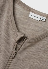 Beige zip-up topp med en texturerad väv, med rund halsringning och sydda kanter. Märket heter "name it" och storlek 1½-2 år.