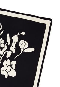Hedvábný šátek s černým pozadím a bílými květinovými vzory a bílým okrajem. Textura je hladká a vzor je výrazný a detailní.