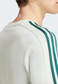 T-shirt grigio chiaro con strisce verticali verdi sulle spalle, scollo a girocollo e morbida texture. Ideale per un look casual.