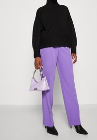 Mustat neuleet turtleneck-paita, violetit leveälahkeiset housut ja vaaleanvioletti krokotiilikuosis laukku, jossa on hopeaketju, yhdistettynä mustiin korkokenkiin.