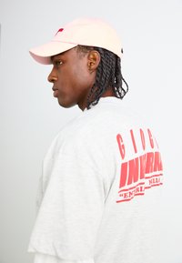T-shirt gris surdimensionné avec du texte rouge au dos, associé à une casquette de baseball rose clair, avec une visière courbée et une sangle ajustable.