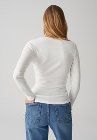 Weißes Langarmoberteil mit einem figurbetonten Design und glatter Textur, kombiniert mit hellblauen Denim-Jeans, die zwei Gesäßtaschen haben.