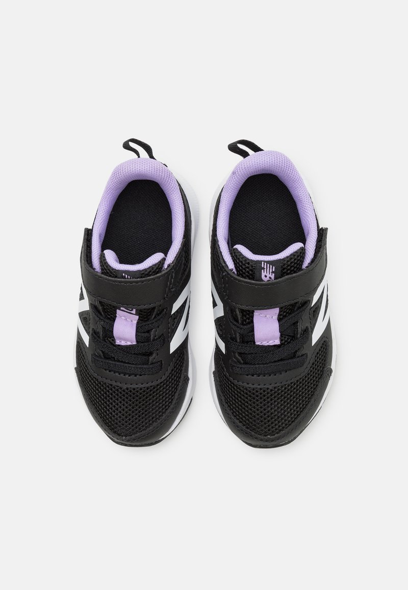 Zapatillas deportivas negras y moradas con material de malla, correa ajustable, acentos blancos y suela texturizada, diseñadas para comodidad y soporte.