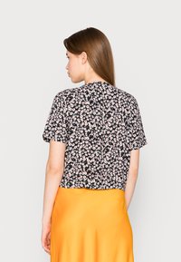 Blusa preta com flores de mangas curtas, apresentando pequenas flores brancas e rosas, combinada com uma saia de cetim amarela brilhante.