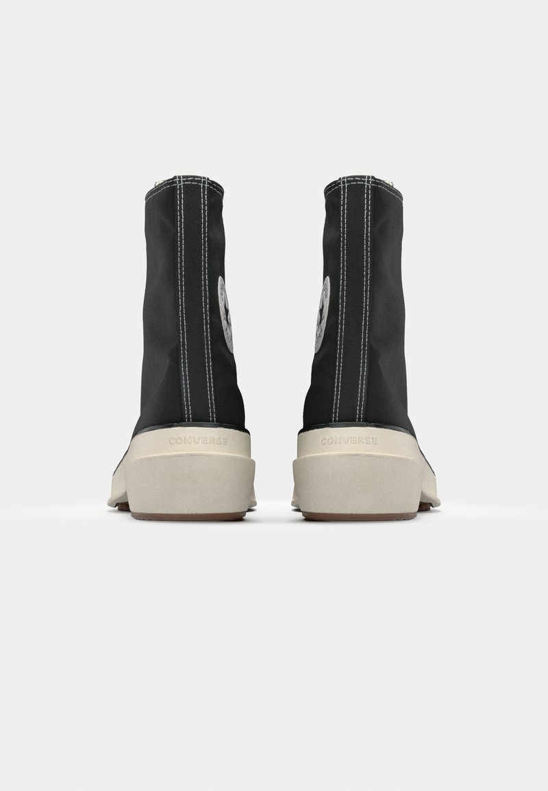 Scarpe da ginnastica alte nere in tela con cuciture bianche e un logo circolare su ciascun lato esterno, dotate di una suola in gomma beige.