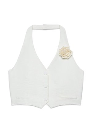 Veste blanche à col halter avec trois boutons et une fleur en tissu épinglée sur la poitrine gauche, avec deux petites poches à l'avant.