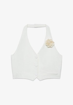 Veste blanche à col halter avec trois boutons et une fleur en tissu épinglée sur la poitrine gauche, avec deux petites poches à l'avant.