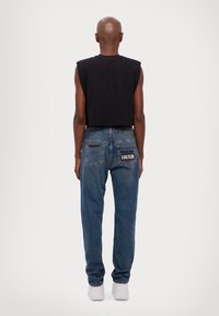 Fekete, rövid, ujjatlan top kék farmernadrággal párosítva, hátul zsebekkel és szöveges részlettel. A farmernadrág enyhén bő szabású.