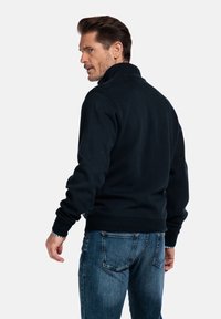 Marineblaues Fleece-Sweatshirt mit hohem Kragen, gerippten Bündchen und Saum. Über hellblauen Jeans getragen, die ein strukturiertes, lässiges Design zeigen.