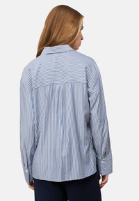 Blue and white striped button-up shirt with a pleated back, long sleeves, and a classic collar. Cotton fabric with a smooth texture.
