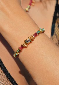 Bracelet en or ornée d'accents en turquoise, rubis et perles, avec un centre en forme de soleil et de délicats détails texturés.