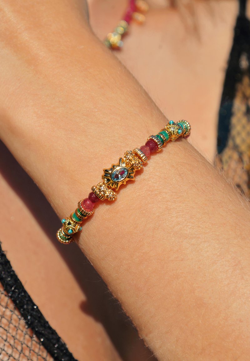 Bracelet en or ornée d'accents en turquoise, rubis et perles, avec un centre en forme de soleil et de délicats détails texturés.