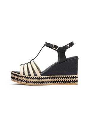 Sandalia de cuña negra y beige con un diseño de tira en T. Presenta acentos de yute trenzado alrededor de la suela y una textura tejida suave en los laterales.