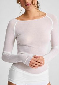 Hosszú ujjú, áttetsző fehér felső, könnyű anyagból, hajónyakú kivágással és kontrasztos fehér varrásokkal a vállaknál és a csukló körül.