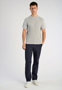 Ανοιχτό γκρι πουλόβερ με κοντά μανίκια και κοτσίδα πλέξης, συνδυασμένο με σκούρο μπλε παντελόνι και λευκά αθλητικά παπούτσια. Απλός σχεδιασμός και μοντέρνα εφαρμογή.