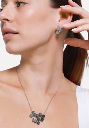 Silbernes Blumenschmuck-Set mit runder, strukturiertem Anhänger-Halskette und passenden Ohrsteckern, vor einem hellen Hintergrund präsentiert.