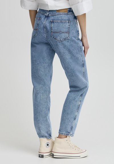 Vaqueros de mezclilla azul claro con un ajuste relajado, que cuentan con una cinturilla, dos bolsillos traseros y una textura ligeramente deslavada. Combinados con zapatillas altas beige.