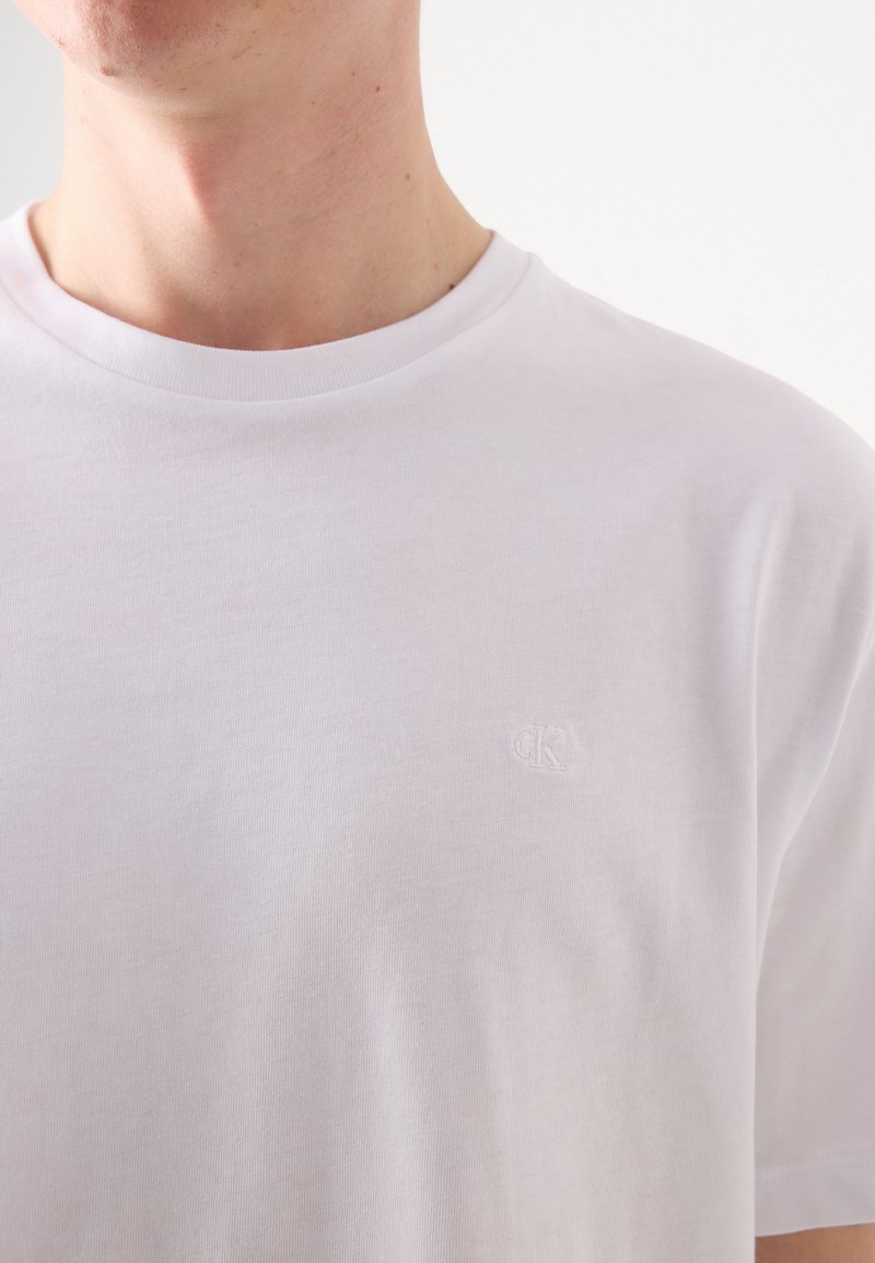 Biała bawełniana koszulka z okrągłym dekoltem i krótkimi rękawami. Dyskretny haftowany logo na piersi. Gładka tekstura.