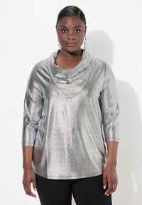 Silberner, metallischer Oberteil mit Cowl-Neck und strukturiertem Muster, mit dreiviertel Ärmeln und lockerer Passform, kombiniert mit schwarzen, enganliegenden Hosen.