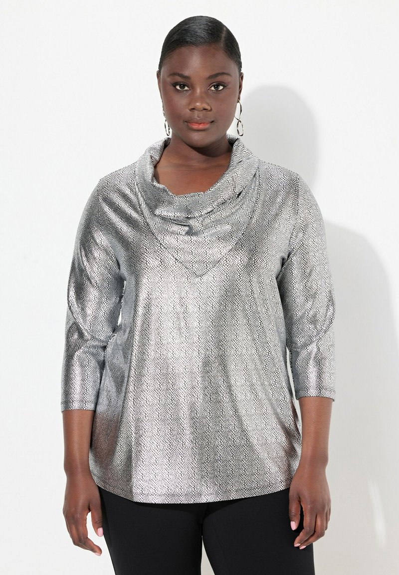 Silberner, metallischer Oberteil mit Cowl-Neck und strukturiertem Muster, mit dreiviertel Ärmeln und lockerer Passform, kombiniert mit schwarzen, enganliegenden Hosen.
