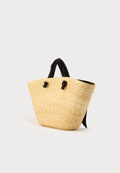 Πλεκτή τσάντα ώμου από ψάθα με μαύρες υφασμάτινες λαβές, διαθέτει ευρύ άνοιγμα, απαλή υφή και στρογγυλεμένο σχήμα. Διακοσμημένη με λεπτομέρειες κόμπων στις λαβές.