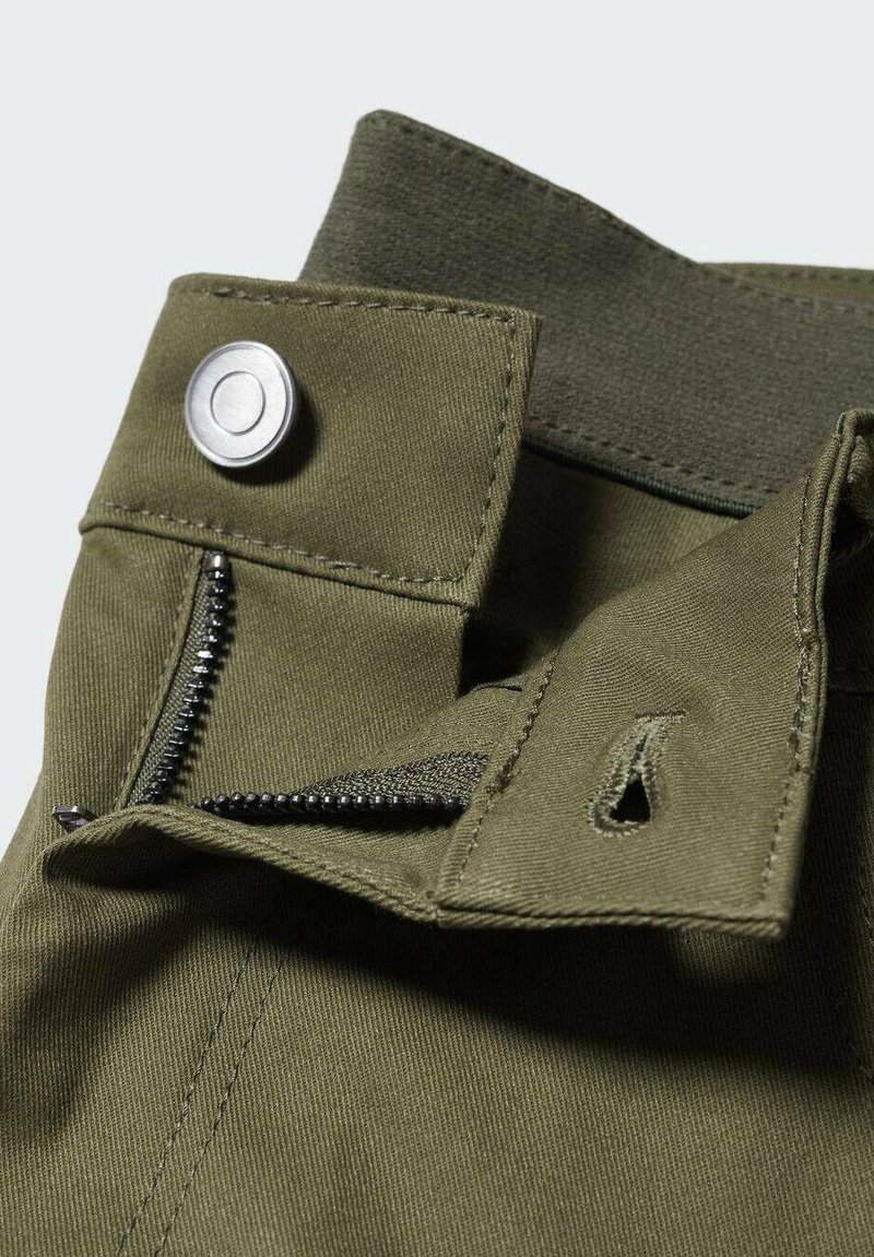 Khakihosen mit einem silbernen Druckknopf, Reißverschluss und strukturierter Stoffqualität mit weicher Oberfläche. Stickdetails sind entlang der Kanten sichtbar.