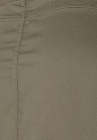 Tissu vert olive avec une texture lisse, présentant des coutures bien marquées le long des joints et un léger éclat. Pas de motifs ou de matériel supplémentaires.