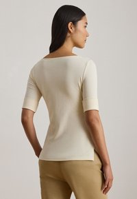 Beige fitted top with a wide neckline and elbow-length sleeves. Smooth texture with seam detailing at the hem and sleeves.
