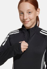 Zwarte sportieve zip-up top van soepel materiaal. Heeft witte strepen op de schouders, duimopeningen in de mouwen en een slim fit ontwerp.