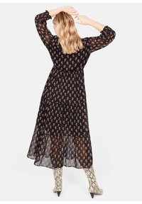 Abito midi nero con motivo paisley beige, caratterizzato da maniche lunghe e orlo a strati. Indossato con stivali alti fino al ginocchio con stampa rettile.