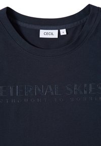 Camiseta de algodón azul marino con cuello redondo y texto brillante "CIELOS ETERNOS" en un acabado contrastante. La etiqueta dice "CECIL" y tamaño "S".