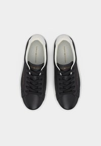 Ζευγάρι μαύρα δερμάτινα αθλητικά παπούτσια με κορδόνια, λευκές σόλες και λογότυπο "Tommy Hilfiger" στις πλευρές και τα εσωτερικά πέλματα, εμφανιζόμενα από πάνω.