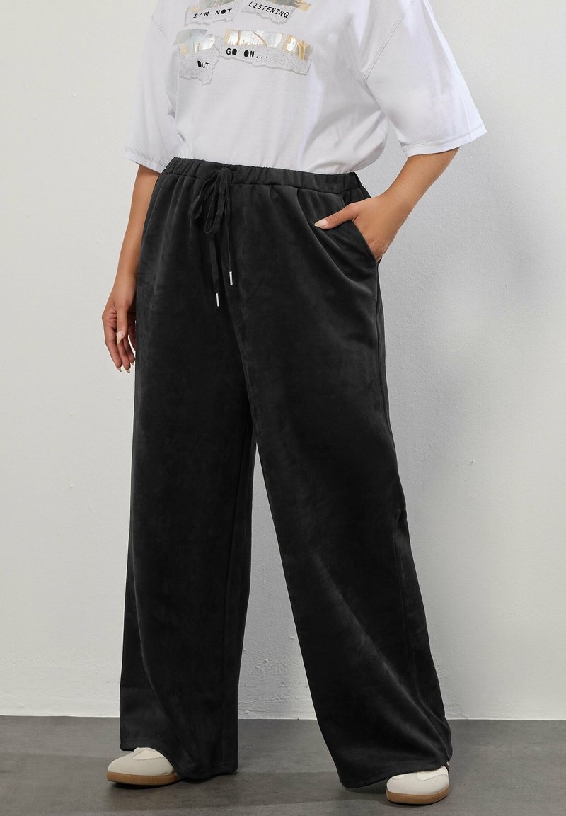 Czarne, szerokie spodnie dresowe wykonane z miękkiego, pluszowego materiału. Posiadają elastyczny pas z troczkami oraz boczne kieszenie.