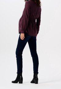 Rødrutede og sorte skjorte med lange ærmer, smocket talje, parret med mørkeblå jeans og sorte ankelstøvler, sat mod en hvid baggrund.