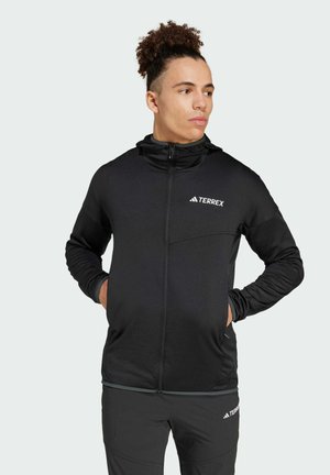 Black Terrex jacket with a zip front, hood, and logo accent. Made of smooth, stretch fabric with a fitted design and pockets.
