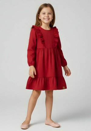 Czerwona sukienka z długim rękawem z falbankami przy dekolcie i warstwową spódnicą. Gładka faktura materiału, długość do kolan, zestawiona z jasnoróżowymi balerinami.