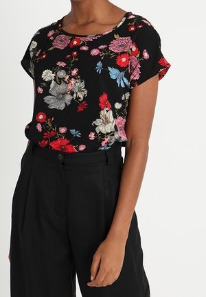 Woman wearing a black short-sleeve blouse with red, pink, blue, and white floral print, paired with high-waisted black pants.