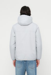 Lys grå pufferjakke med hette, glatt tekstur, elastiske mansjetter og rett kant, brukt over lyseblå denimjeans.