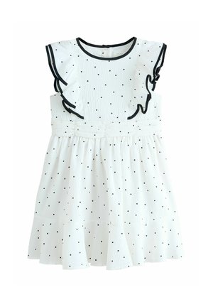 Hvid ærmeløs kjole med sorte polkaprikker, flæser på skuldrene, sort kant og en samlet talje til en piges påklædning.