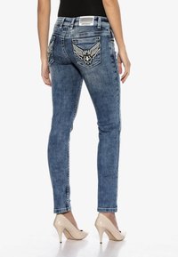 Eng anliegende blaue Jeans mit bestickten Flügelmotiven auf den Gesäßtaschen, leichter Used-Optik, mittelblauer Waschung und klassischem Fünf-Taschen-Design.