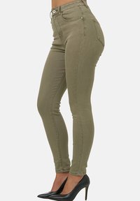 Jeans skinny verde oliva hechos de una mezcla de algodón, con cierre frontal de botón, pasadores para cinturón y dos bolsillos traseros.