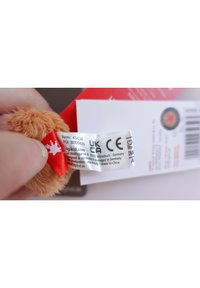 Soft, tan plush toy with a red tag showing item details and care instructions. Tag includes UKCA and CE certification labels.