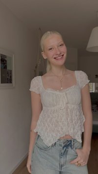 Balta mežģīņu blūze ar kaklasaiti priekšpusē, īsām piedurknēm un viļņotu apakšmalu. Kombinēta ar gaisīgi zilām džinsi ar augstu jostasvietu.