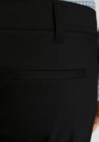 Svarta byxor med en bakficka som har en horisontell flik och en slät yta. Tyget verkar robust och väl sydd.