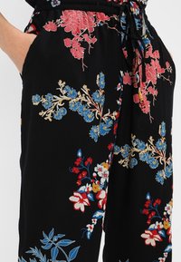 Zwarte stoffen broeken met levendige bloemembroidery in rood, blauw en geel. Elastische tailleband met trekkoord en zijzakken.