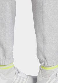 Harmaat collegehousut, joissa on joustavat hihnat, on yhdistetty valkoisiin lenkkitossuihin. kirkkaan keltavihreät yksityiskohdat sukissa näkyvät kengän yli.